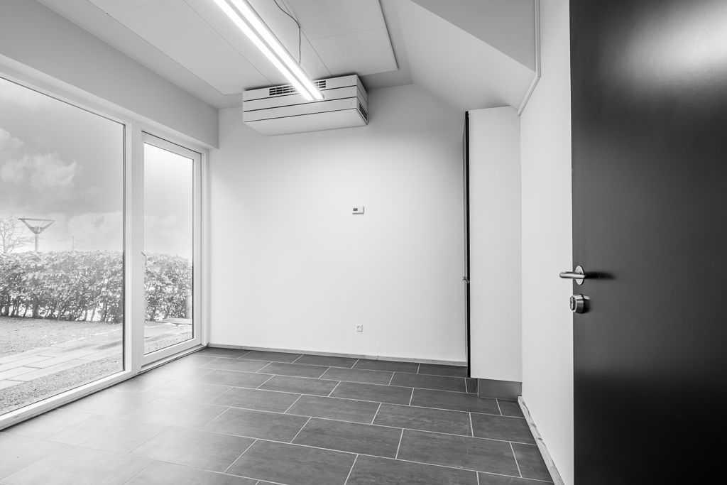 En køkkenafdeling med åbne ruder og en større tøjvask. Der er en køleskab, et varmeapparat og en dør, der vender mod en