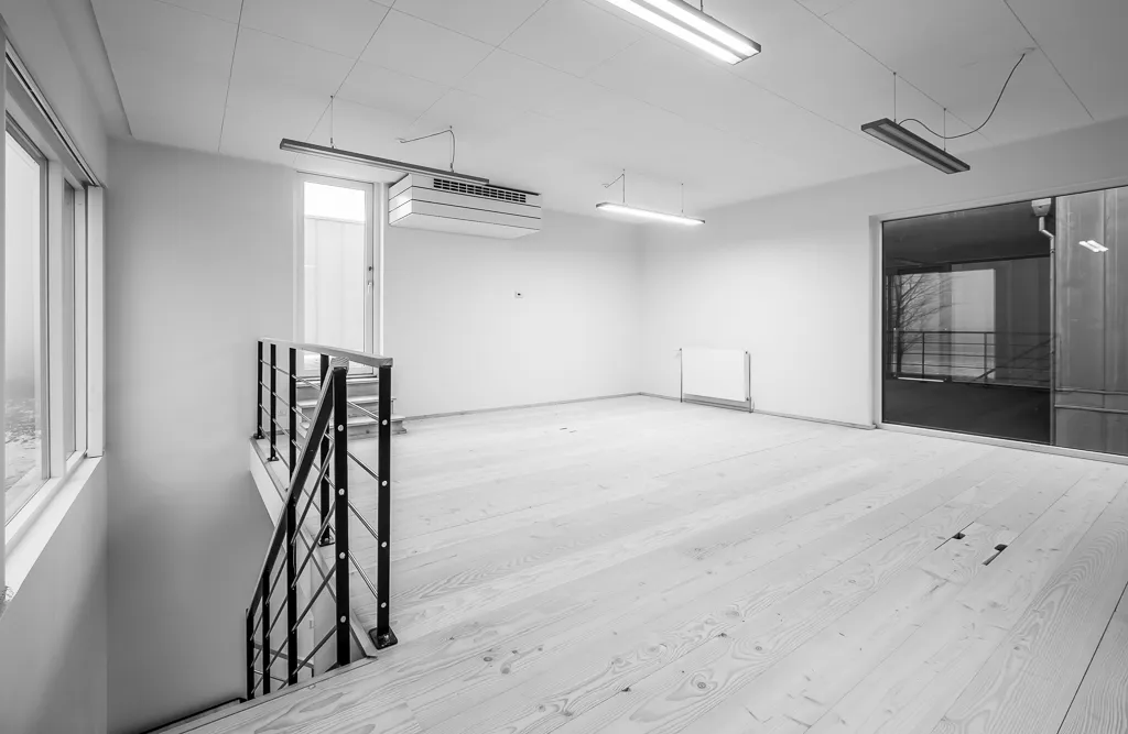 Et rum med et loft, hvor der er et hængende klimaanlæg, og gulvet er lavet af træ. Der er også vinduer med glas og et