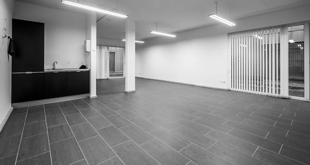 Moderne køkken med lyse loftslamper, hvide vægge, krydsfinerbelagt gulv og en enestående mængde plads. Det er en del af et