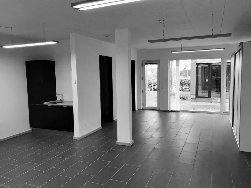 En stor, tom bygning med lysegule vægge og gulvtæppe med åbne døre og vinduer mod en parkeringsplads