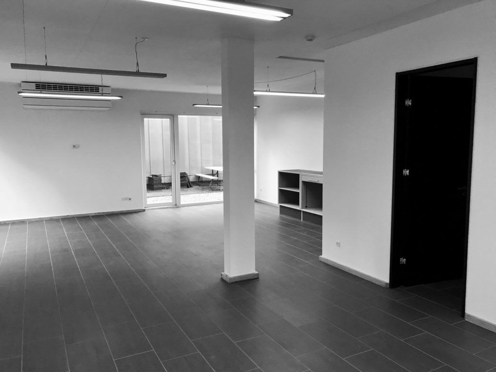 Hjørnekontor med glasdøre og slanke, hvide søjler i et rum med lyse loftslampe og tømmergulve