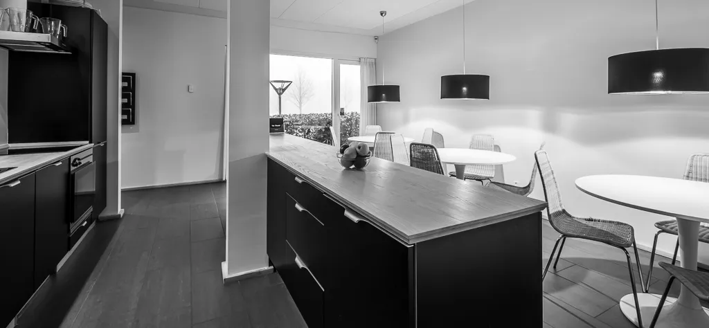 En moderne køkken med køkkenhøj og spisebord med stole, alle i sorte og hvide farver, lysekroner og trægulve