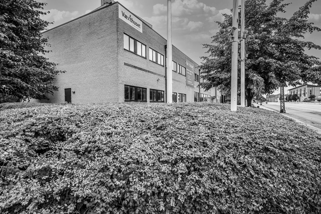 Et stort kontorbygning med høj buske og træer bagved, samt et stort skilt med teksten Vaexthuset