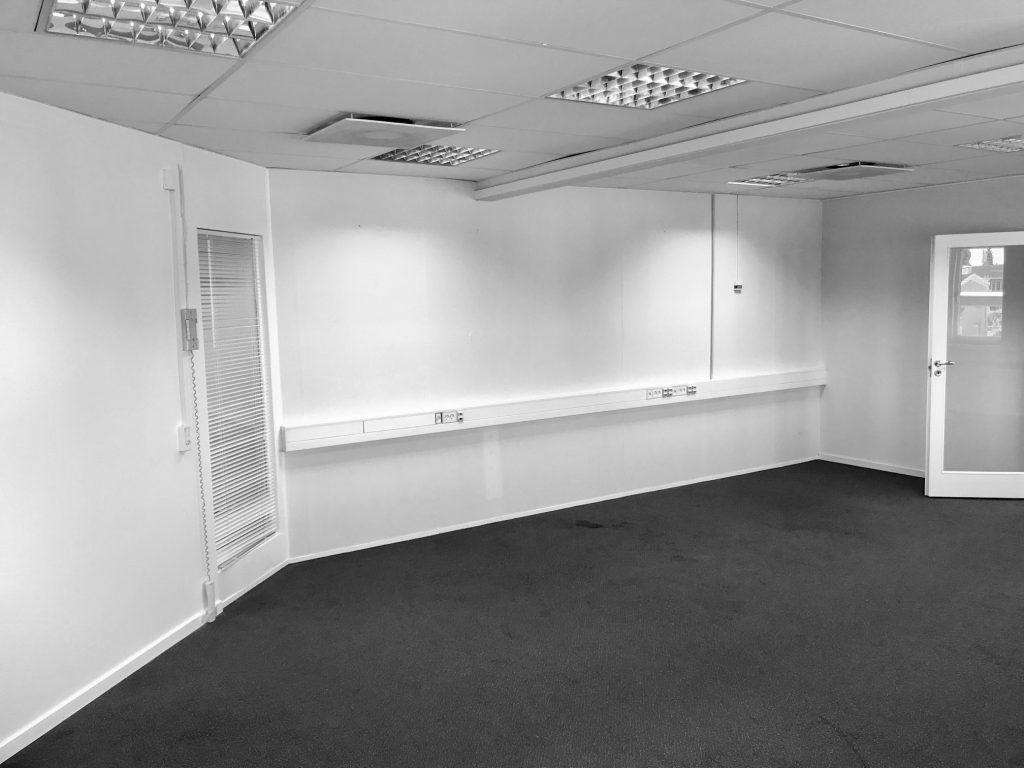 Et tomt kontor med hvide vægge og højt til loftet. Værelset har lyse gulve og høj kvalitet. En hvid dør med ruder og en hvid