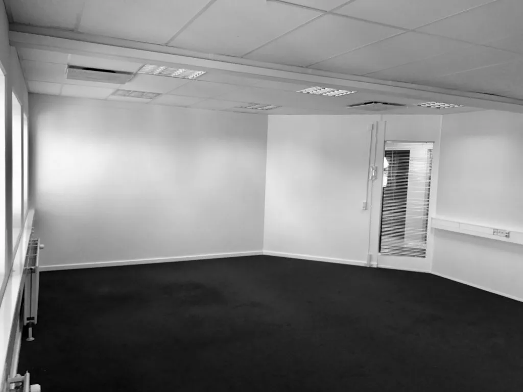 Det tomme kontorrum med hvide vægge og sort gulv har vinduer, hvide lofter og flere radiatorer på væggen.