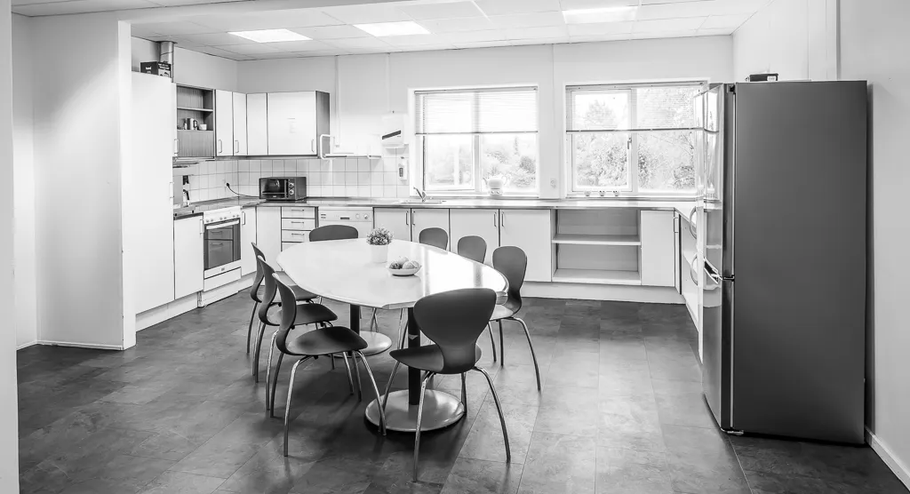 En moderne køkken med en stor rund spisebord og lyse hvide vægge og lofter med indbygget lys.