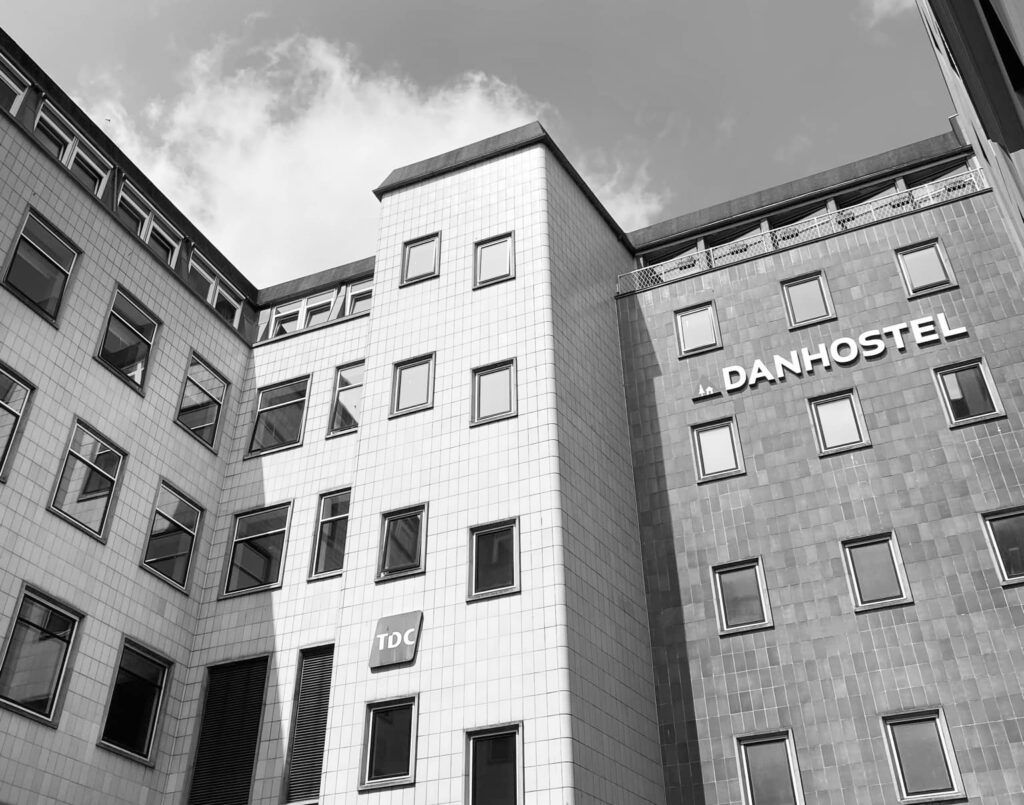 Et højhus med to etager, hvor den ene etage er udstyret med vinduer og et tekstfelt med "TDC" og "Danhostel" i hvidt og sort