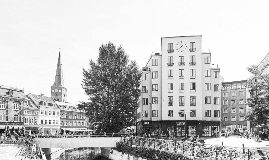 Et hus med et ur på facaden og en bro foran med cykler parkeret og gående mennesker