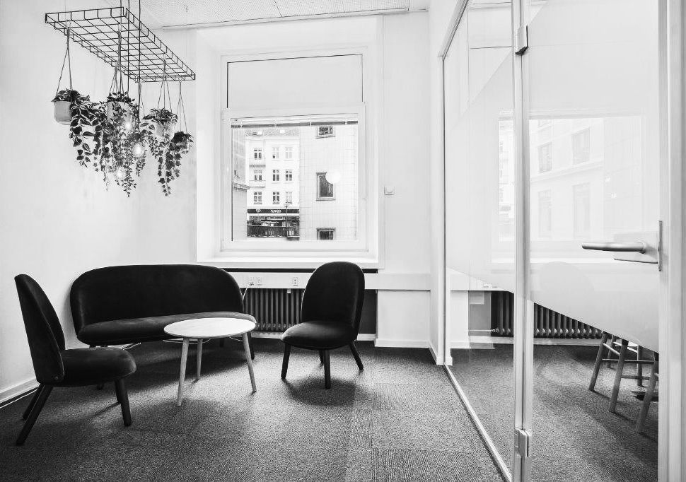 Kontor med sofa og bord i et moderne interiør med højt lys og glasvægge