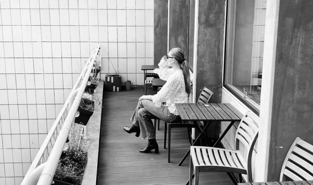 En kvinde sidder på en balkon og drikker fra en kop og nyder udsigten