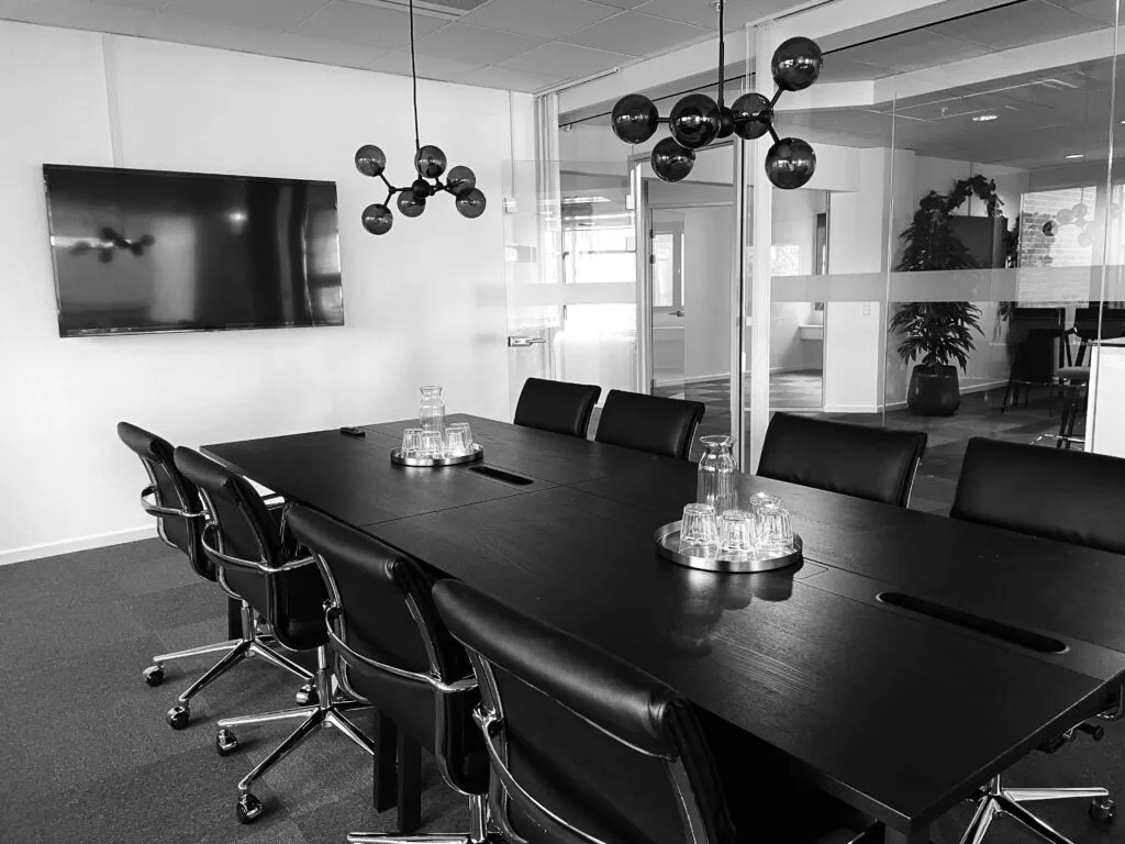 Kontorlokaler med møbler og borde til møder, hvor der er teknologisk udstyr og en plante i glas.