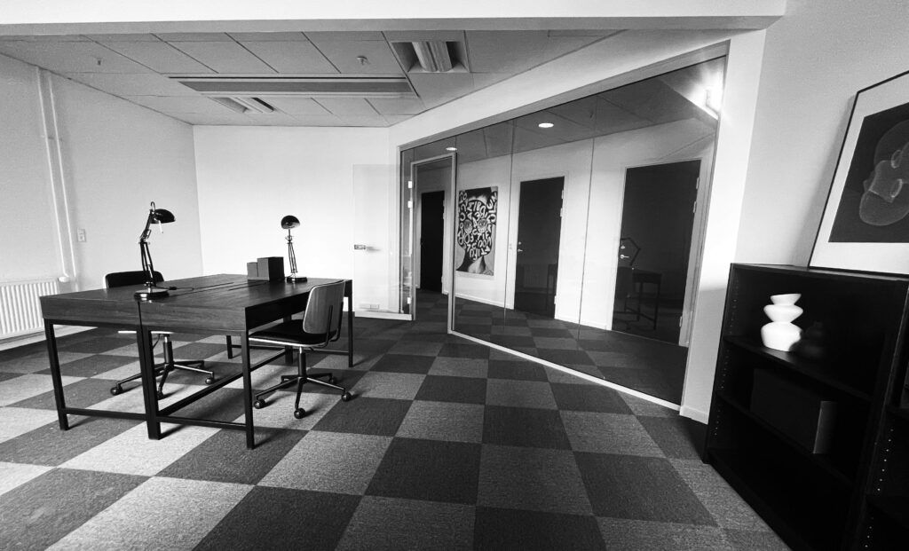 Kontor med skrivebord og stole samt et lille bord med to lamper og en statue