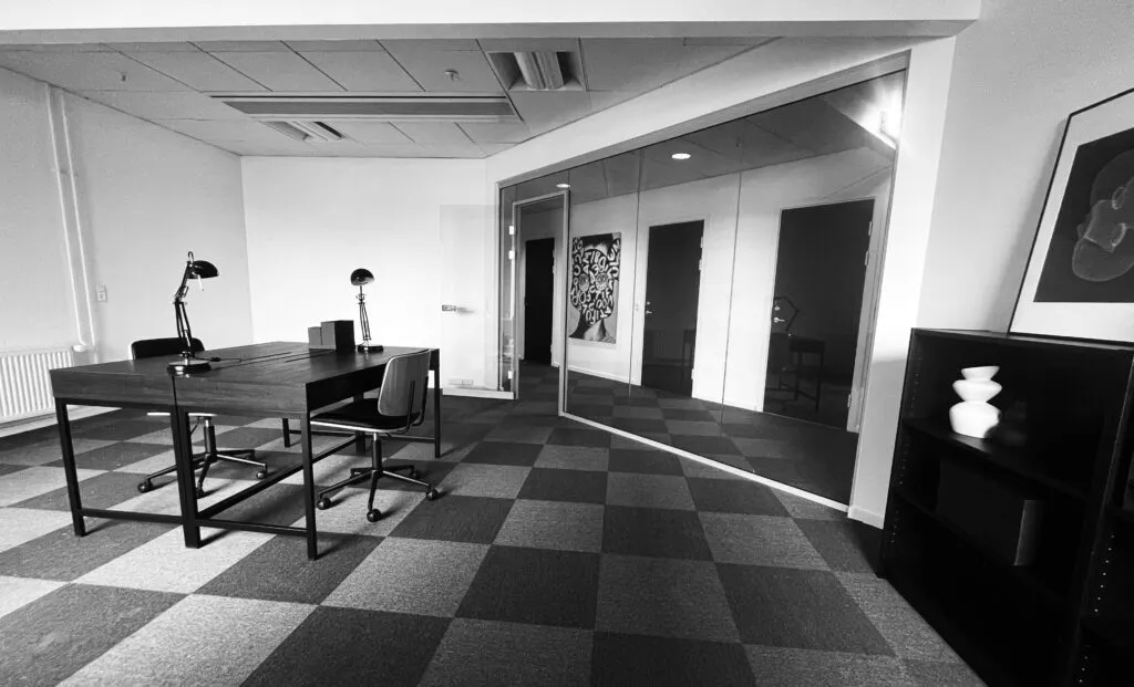 Kontor med skrivebord og stole samt et lille bord med to lamper og en statue