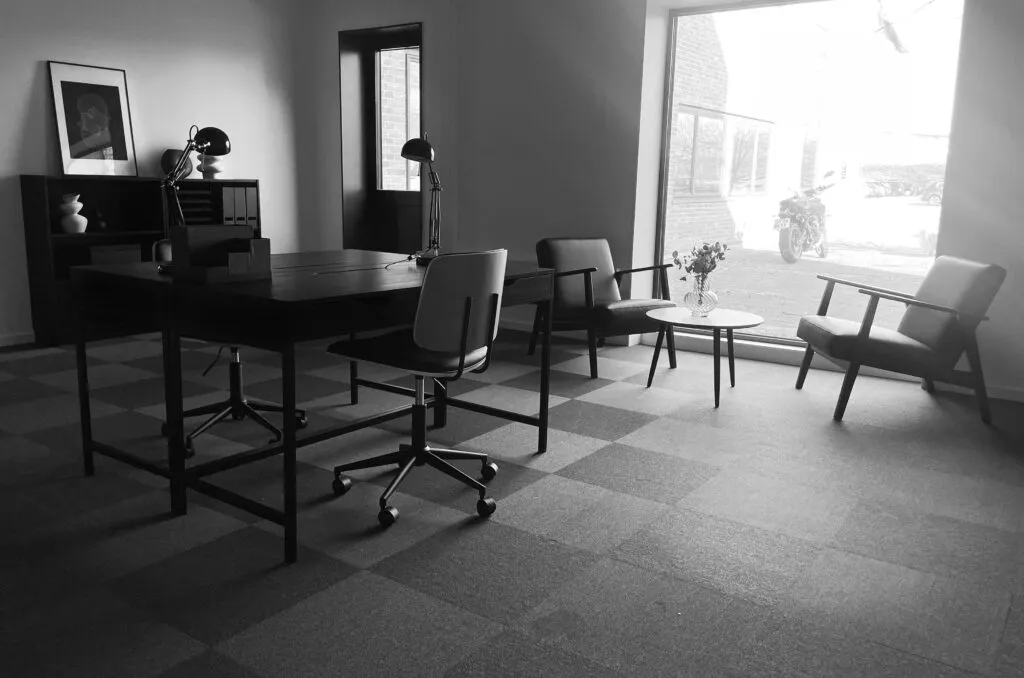 Kontor med moderne møbler og lysegulv. Der er et bord med to stole, der vender mod et vindue med udsigt til en motorcykel og