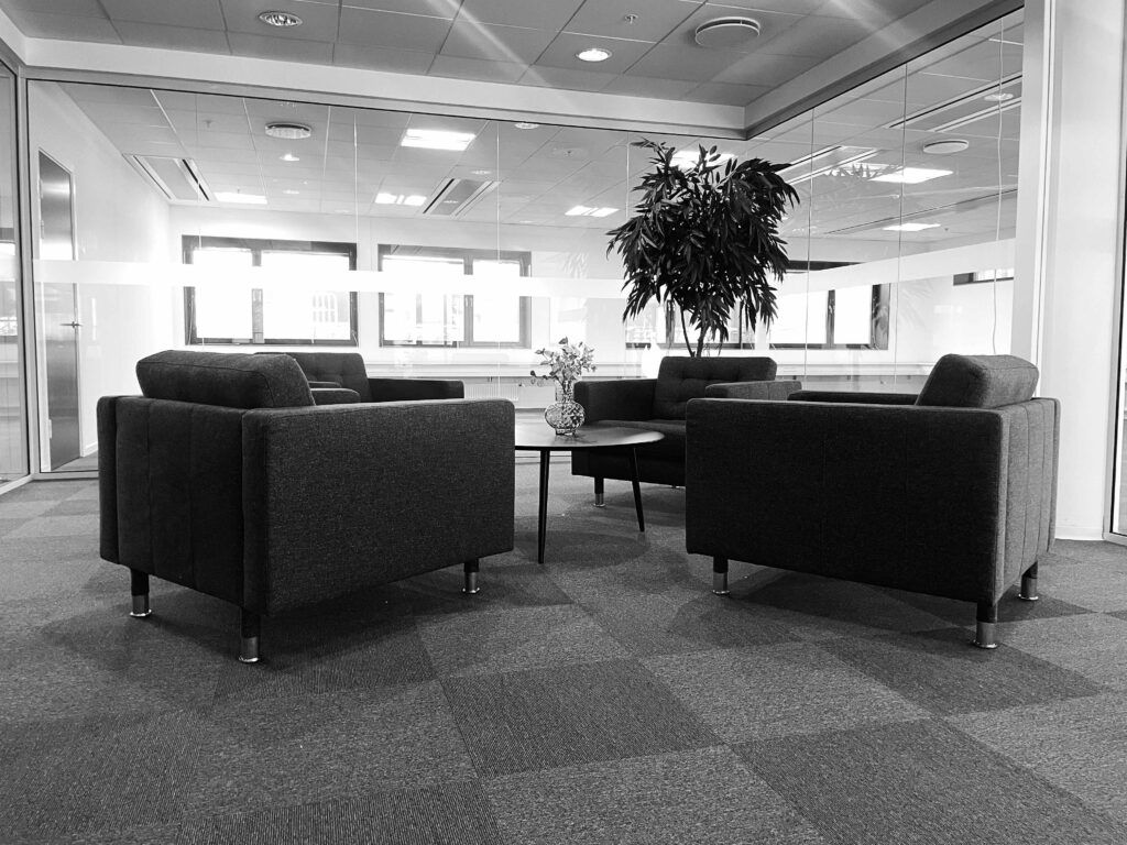 Kontorlokaler med moderne møbler og plante, glasvægge og vinduer, der giver masser af lys.