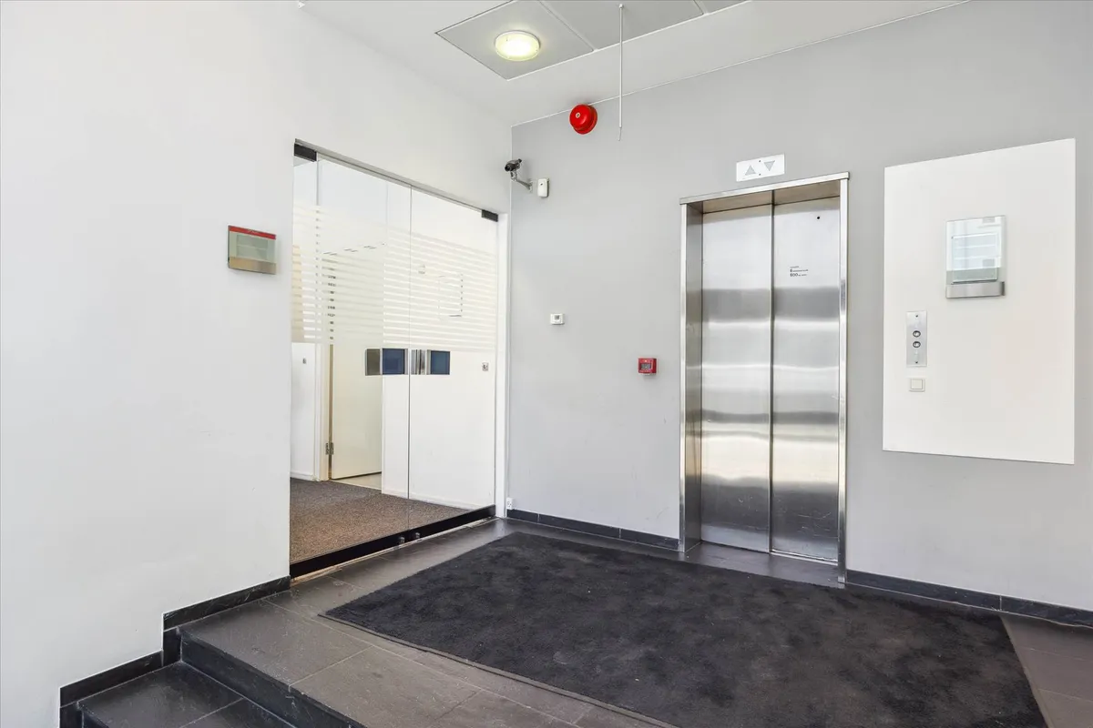 Kontorforretningslokaler med moderne indretning, to elevatorer, glasdøre, hvidt og gråt interiør, rødt alarmknapper og