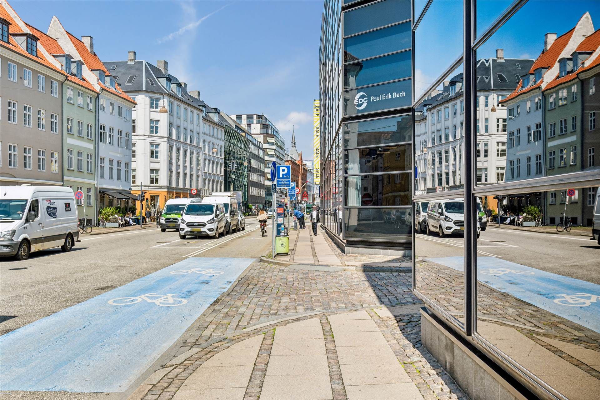 Vandrette cykelfelter og bygninger med røde tag på gade i København, samt biler og folk i baggrunden