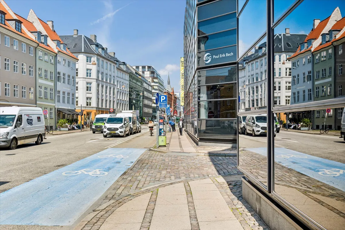 Vandrette cykelfelter og bygninger med røde tag på gade i København, samt biler og folk i baggrunden