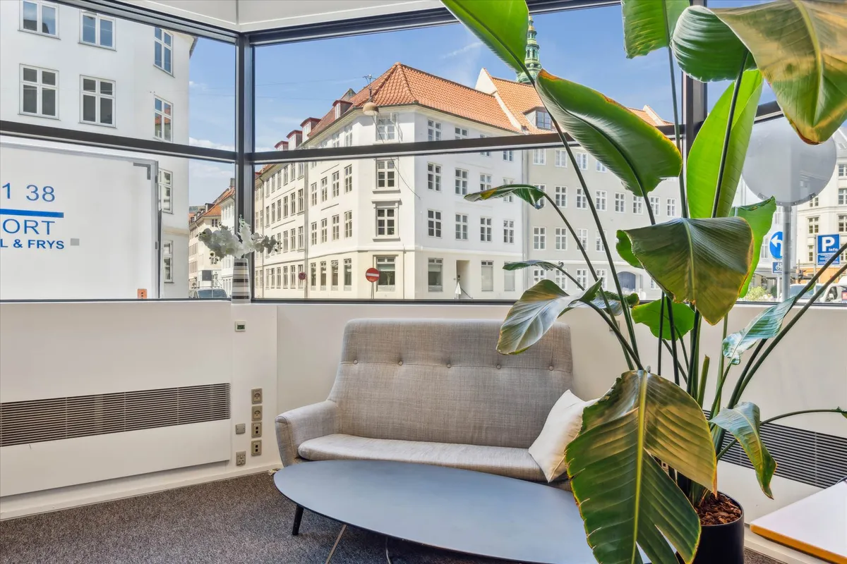 Kontorlokaler med stol, bord, plante og en stor vinduesudsigt til bygning og gadeblik med skilt for Port & Frys