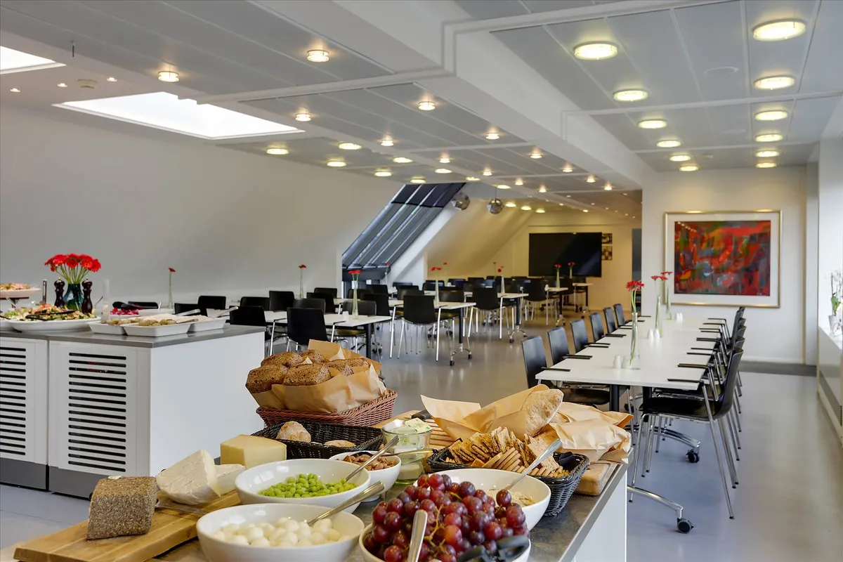 Køkken med forskellige madretter, især grønne bønner, røde druer og brød i en stol, hvor et maleri er hængende på væggen