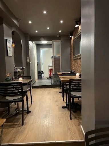 Et moderne restaurant med lyse lofter og trægulve. En række stole og borde med stearinlys. En stol med et glas og et