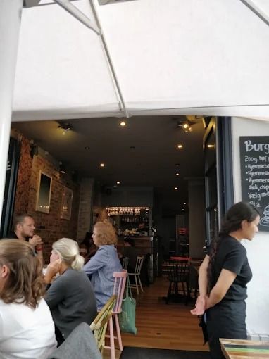 Folk sidder og taler i et caférestaurant med en menutavle med hamburger og øl i baggrunden