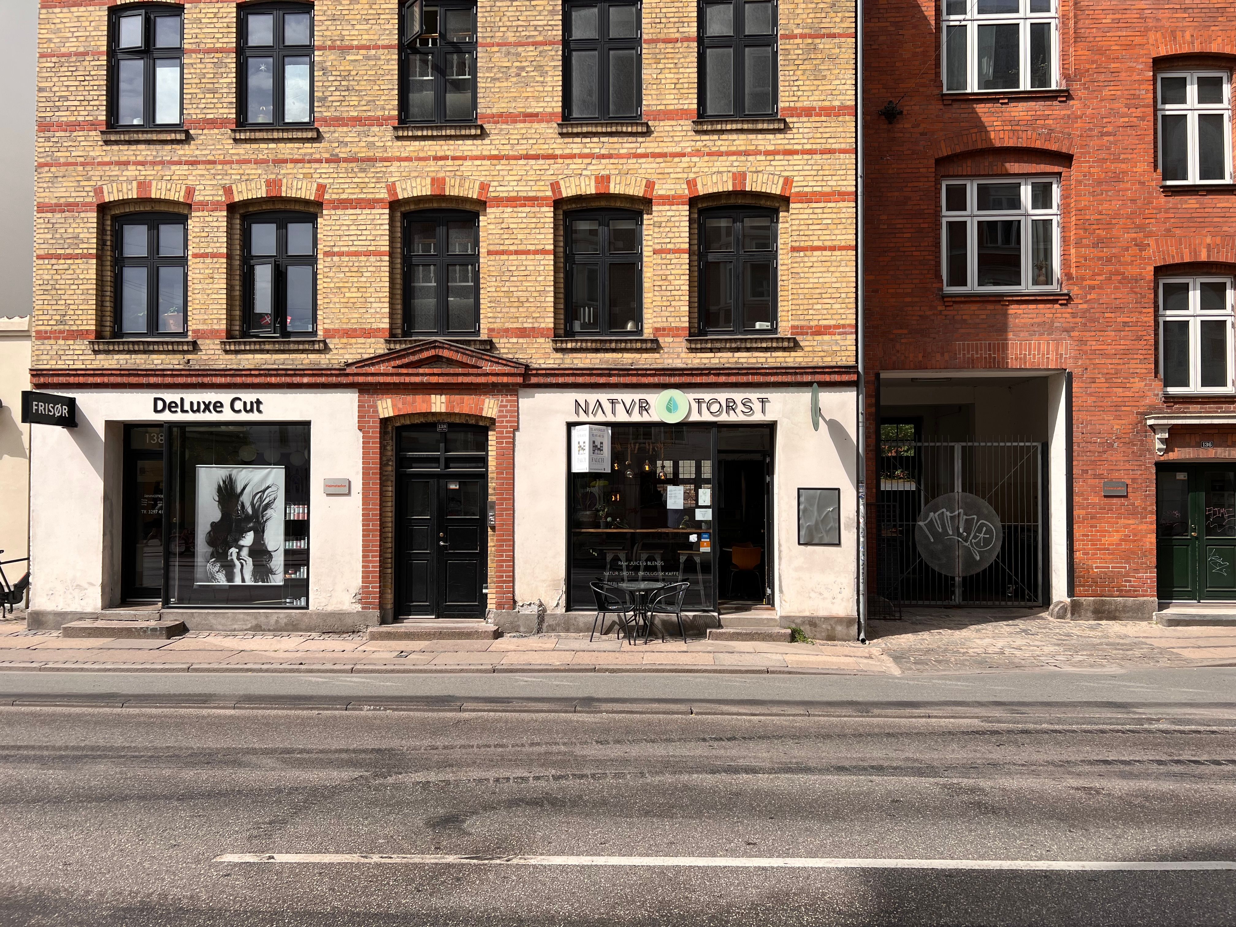 Foto af to bygninger med små butikker og udskæringer i facaderne og vinduer med skrå vinkler og røde rækker