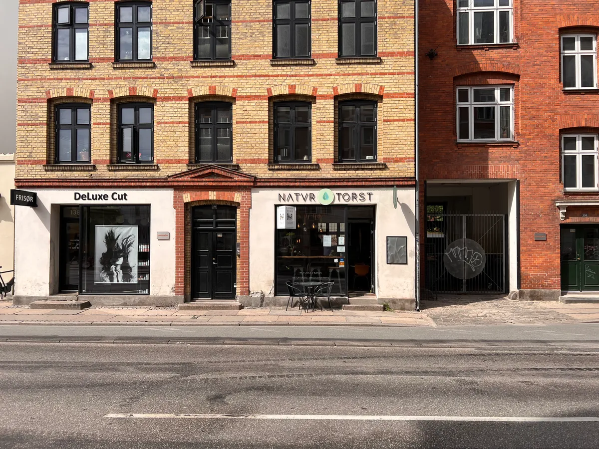 Foto af to bygninger med små butikker og udskæringer i facaderne og vinduer med skrå vinkler og røde rækker