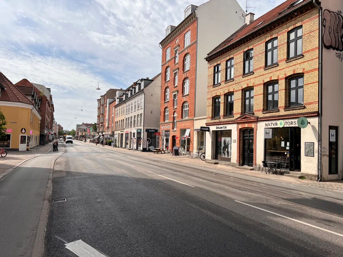 En tom vej med butikker og caféer, hvor der er træer, cykler og en stol med en avis på siden