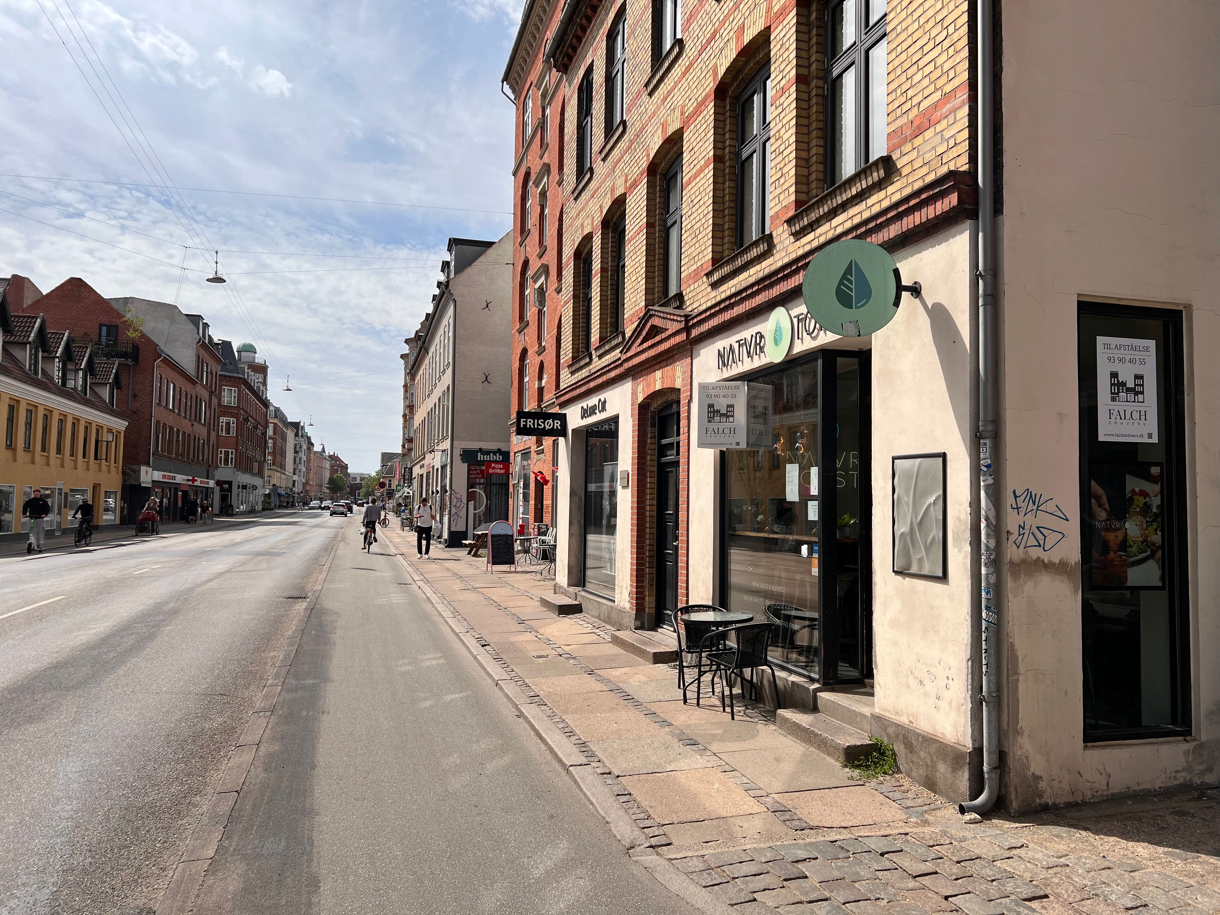 Amagerbrogade er en travl gade med en bygning, der rummer et café med et rundt skilt med grøn logo og tekst, der læses