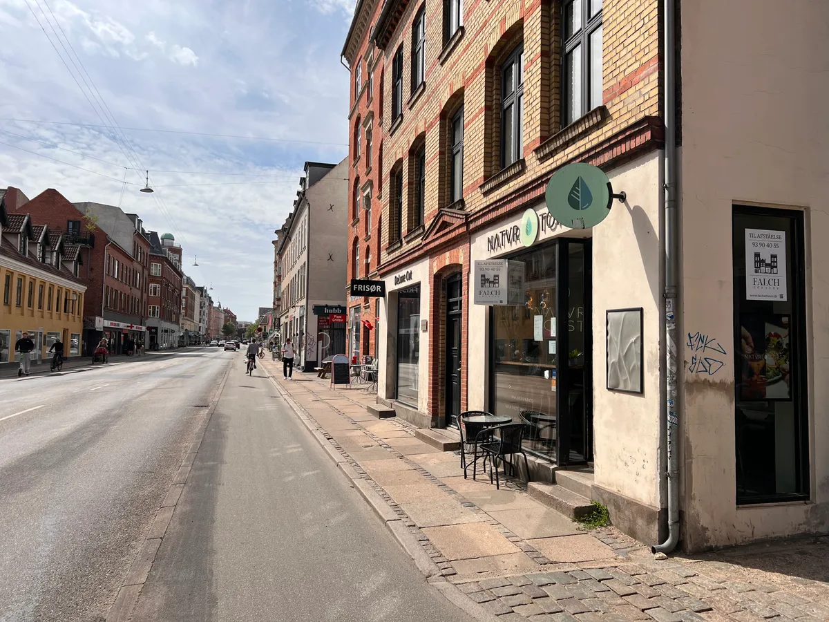 Amagerbrogade er en travl gade med en bygning, der rummer et café med et rundt skilt med grøn logo og tekst, der læses