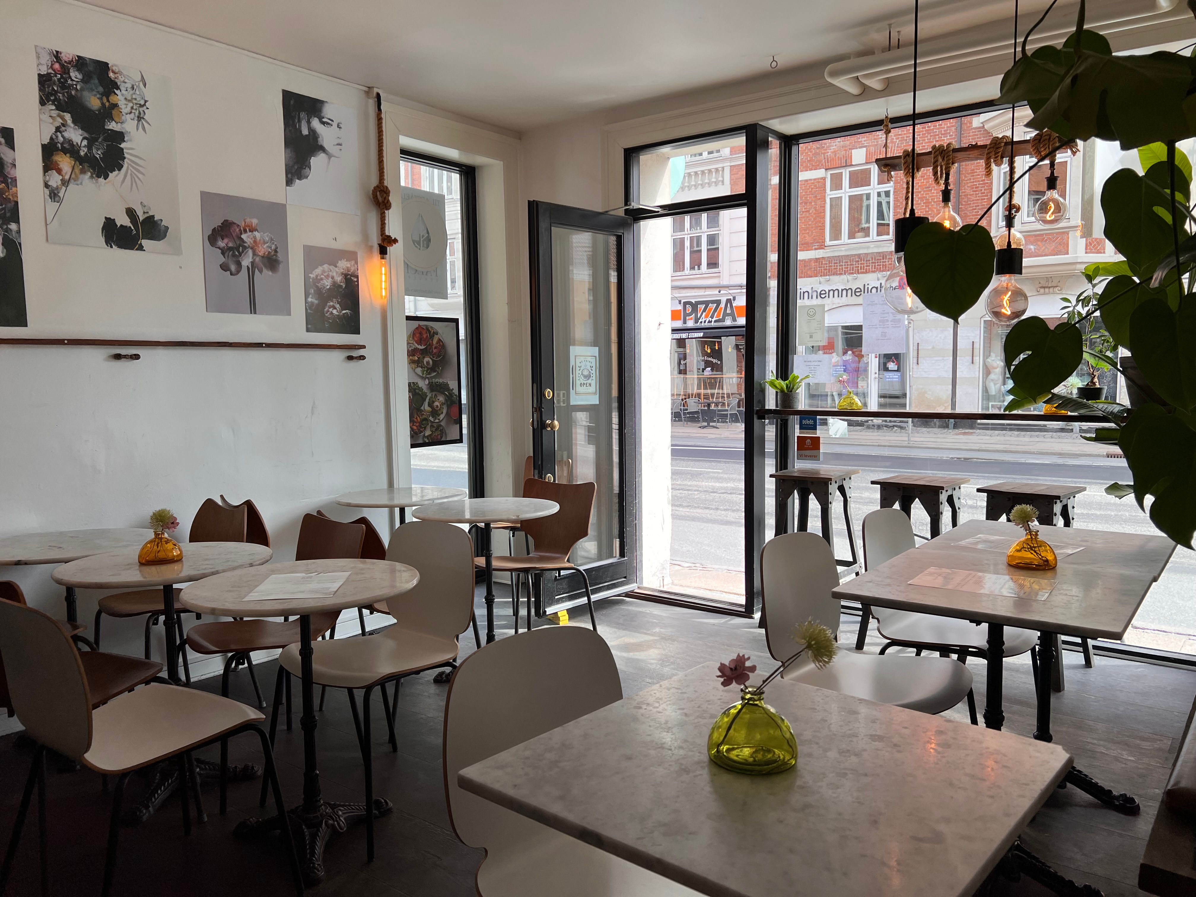 Værelse med marmorborde og hvide stole samt plante og lamper i vinduet, dekoreret med kunst og lyse pærer