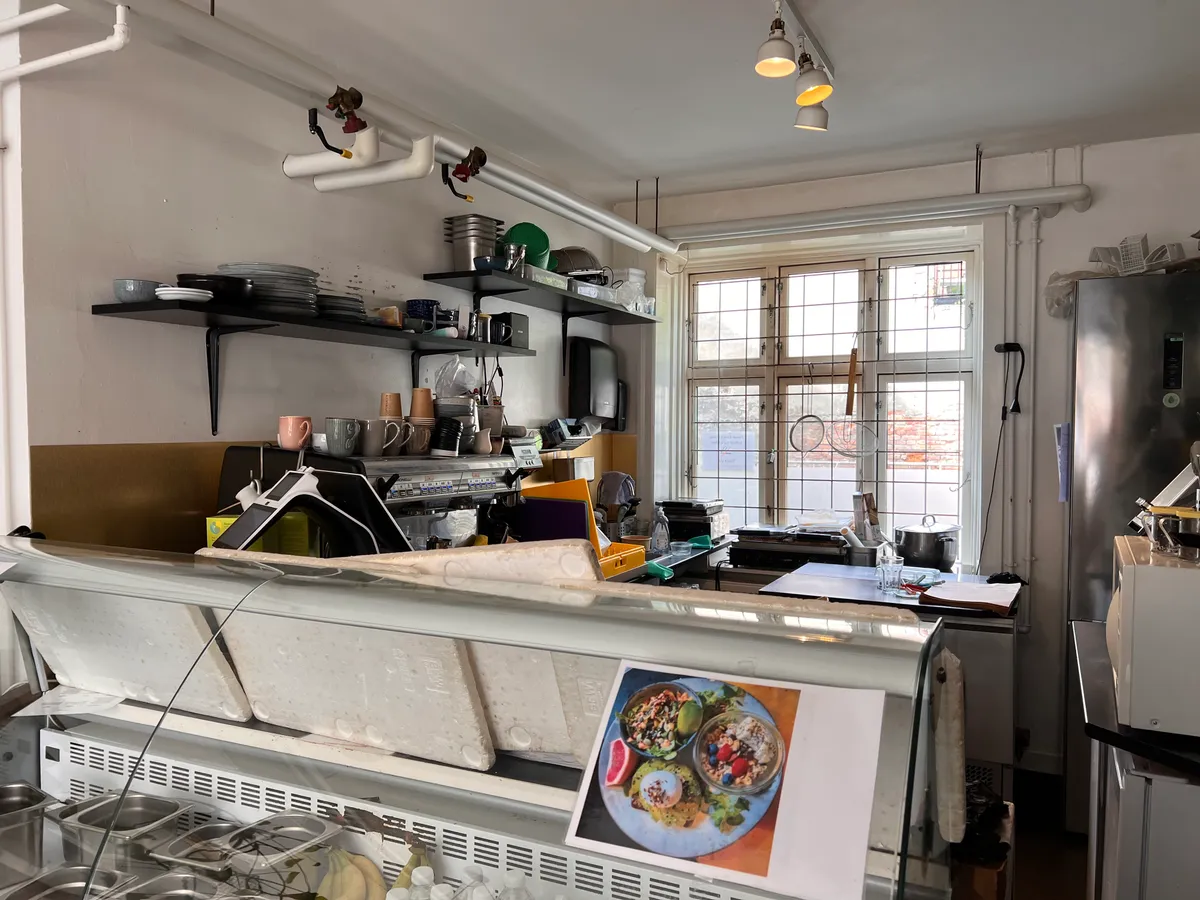 Køkken med lyse hjørder, vinduer, hængende gryder, kaffemaskine, og flere bordplade med madprøver