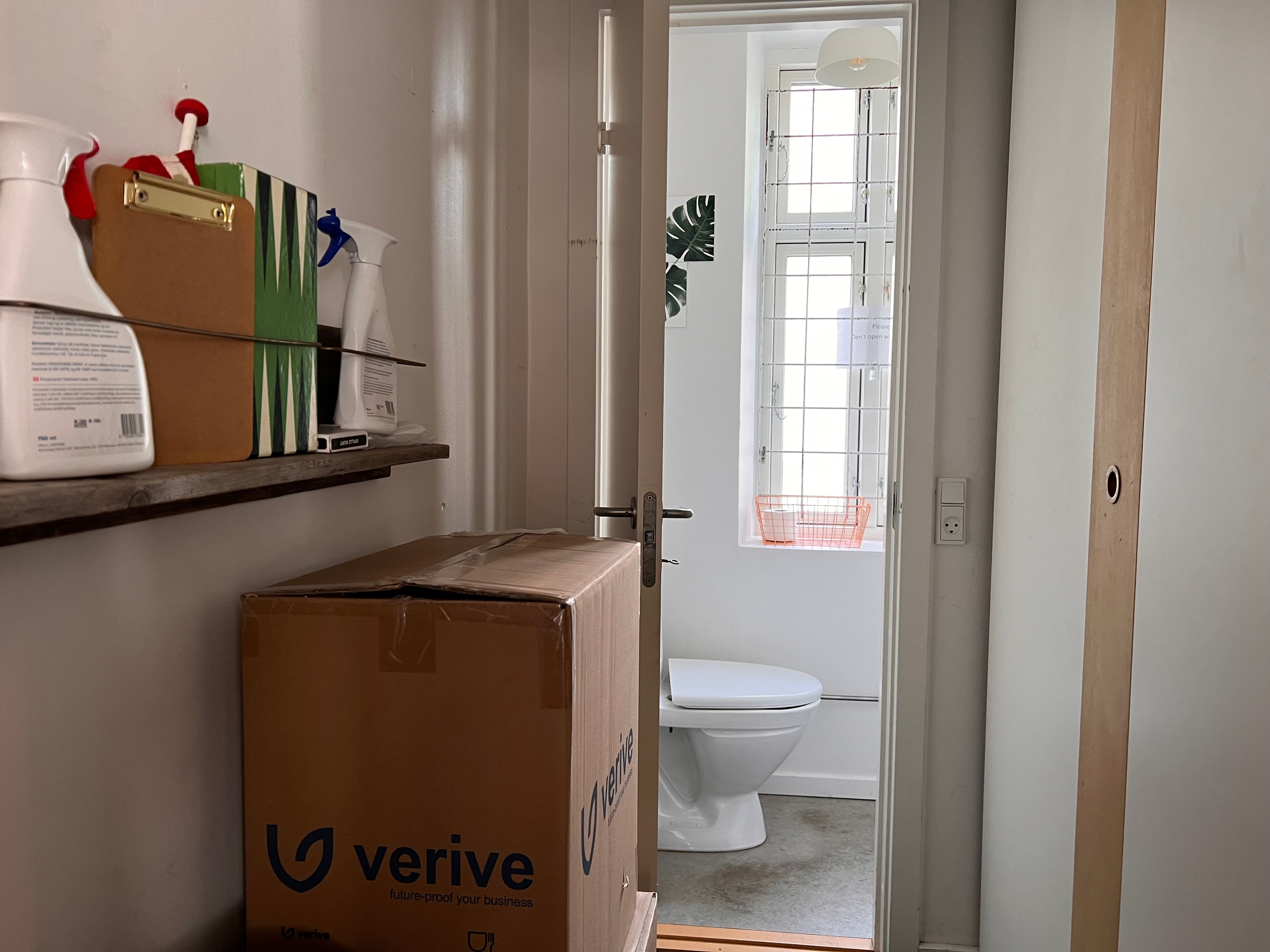 Lejlighed med toilet og lagerrum med Verive-kasser, tørrere, sprayflasker og papkasser på hylden