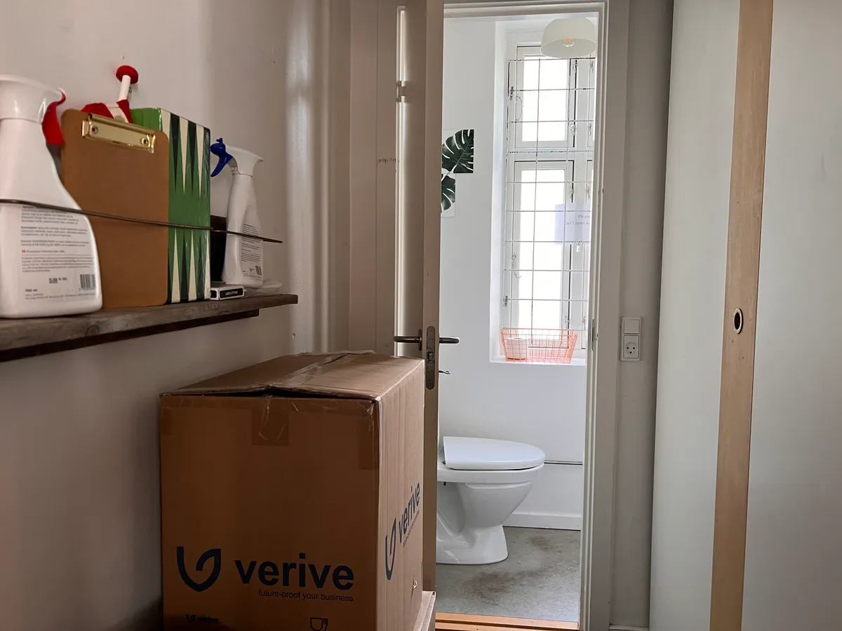 Lejlighed med toilet og lagerrum med Verive-kasser, tørrere, sprayflasker og papkasser på hylden