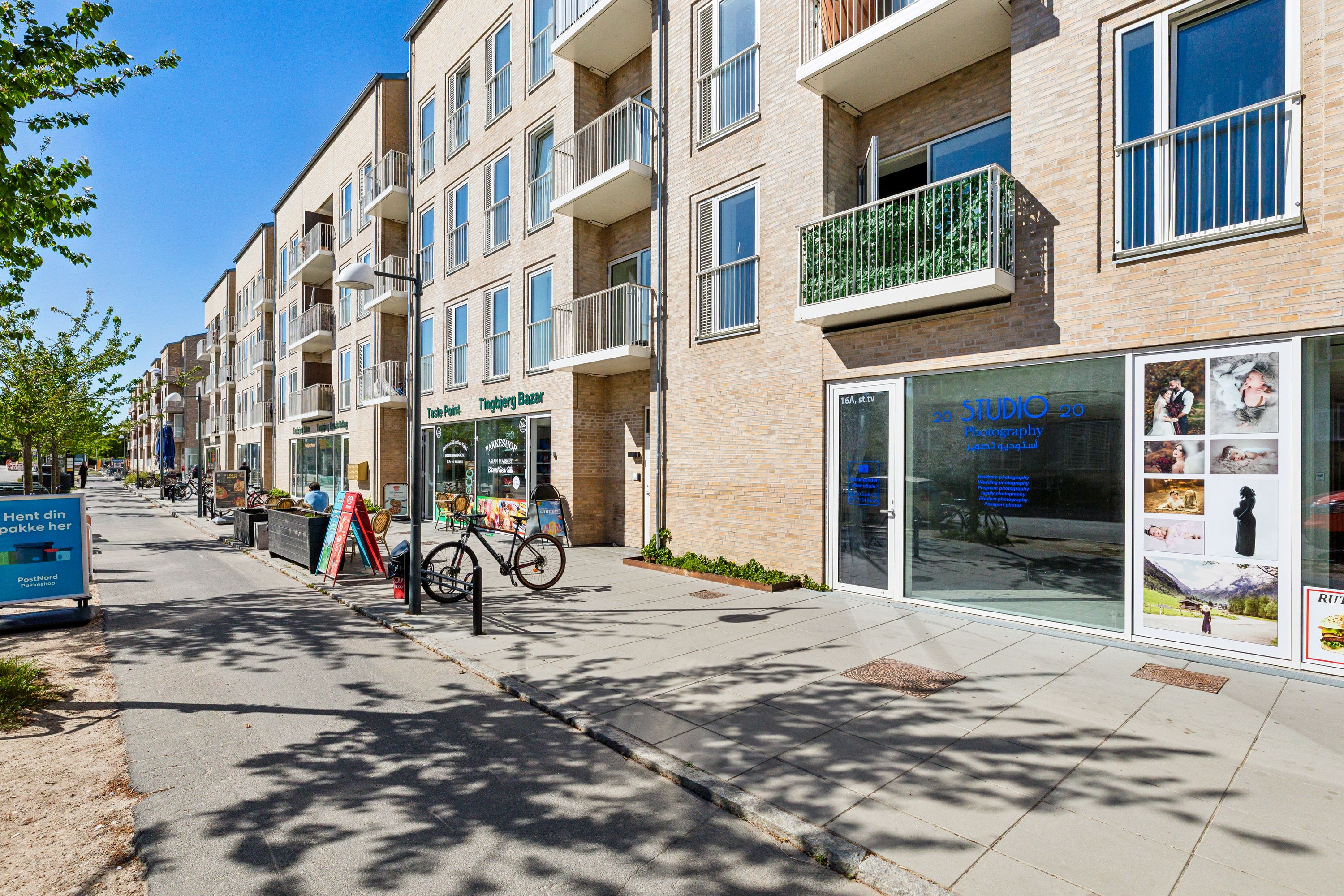 Butikslokal med glasfront og teksten Studio 20. Et enkelt cykelstativ uden cykel og en plantepotte uden plante. En mand