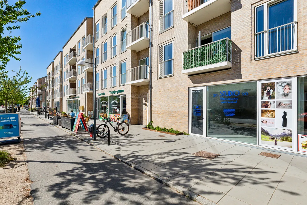 Butikslokal med glasfront og teksten Studio 20. Et enkelt cykelstativ uden cykel og en plantepotte uden plante. En mand