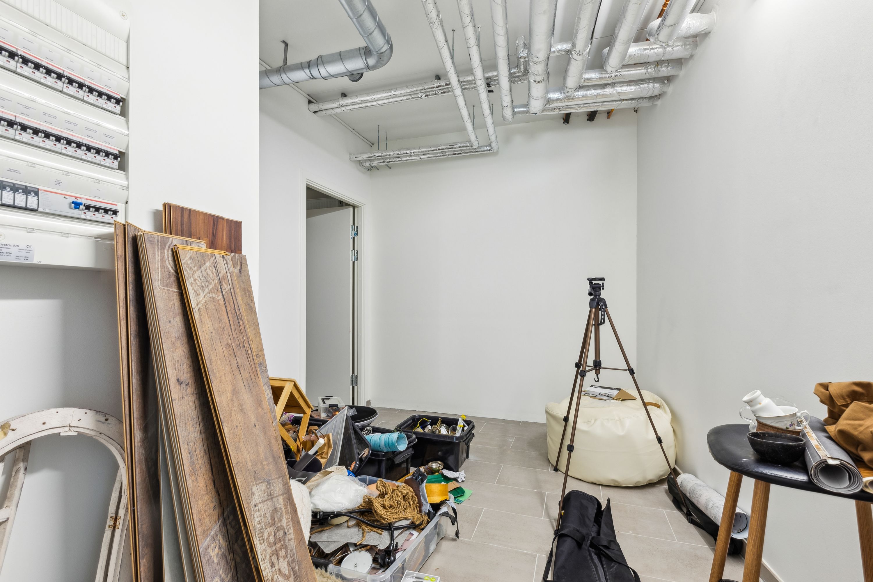 En oplagret lokale med diverse skrald, en hvid sækpose, et stativ og et bord med en kuglekrus