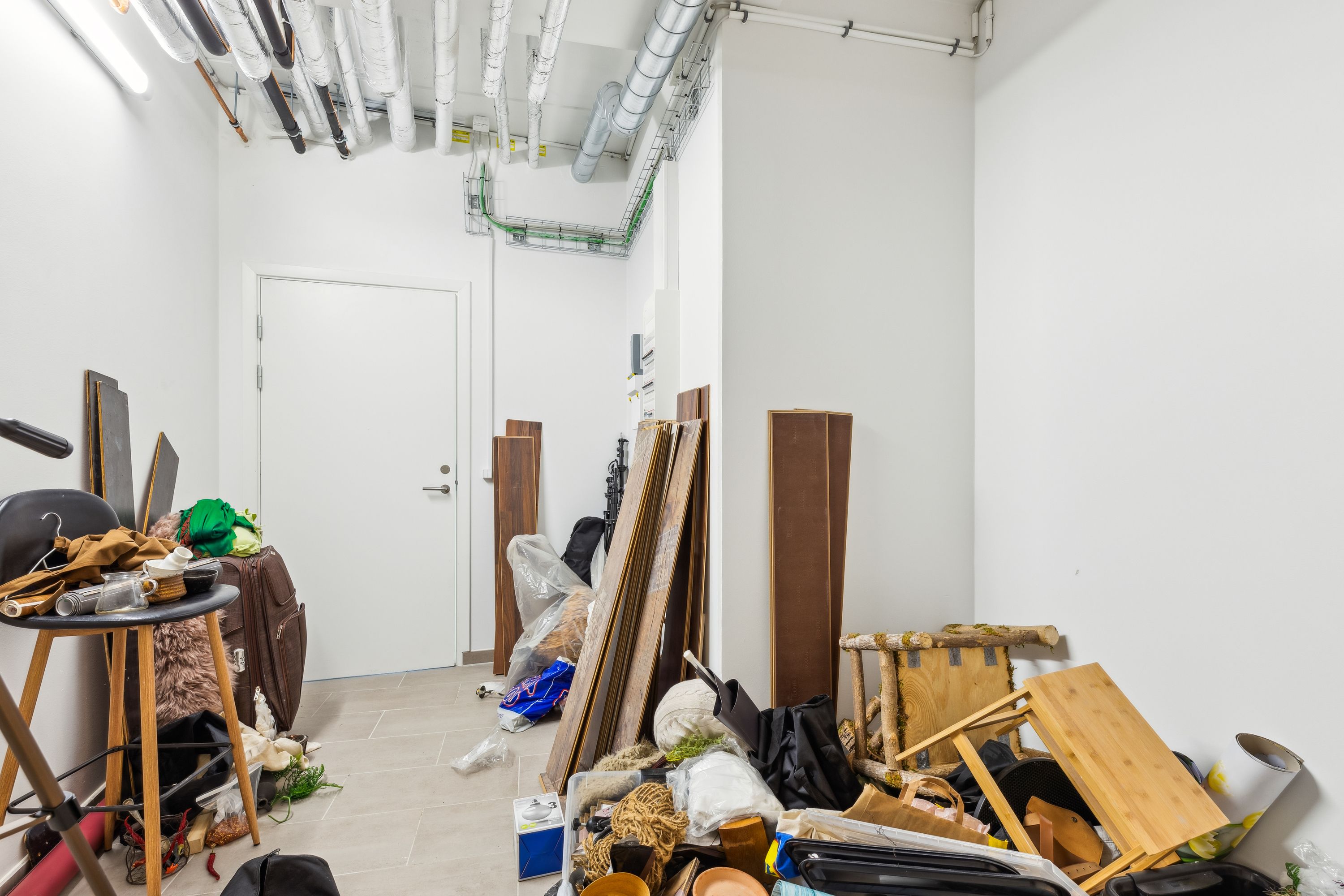 En rummelig og ubenyttet lagerrum med snavsede møbler og diverse genstande som sække, kufferter og glasflasker