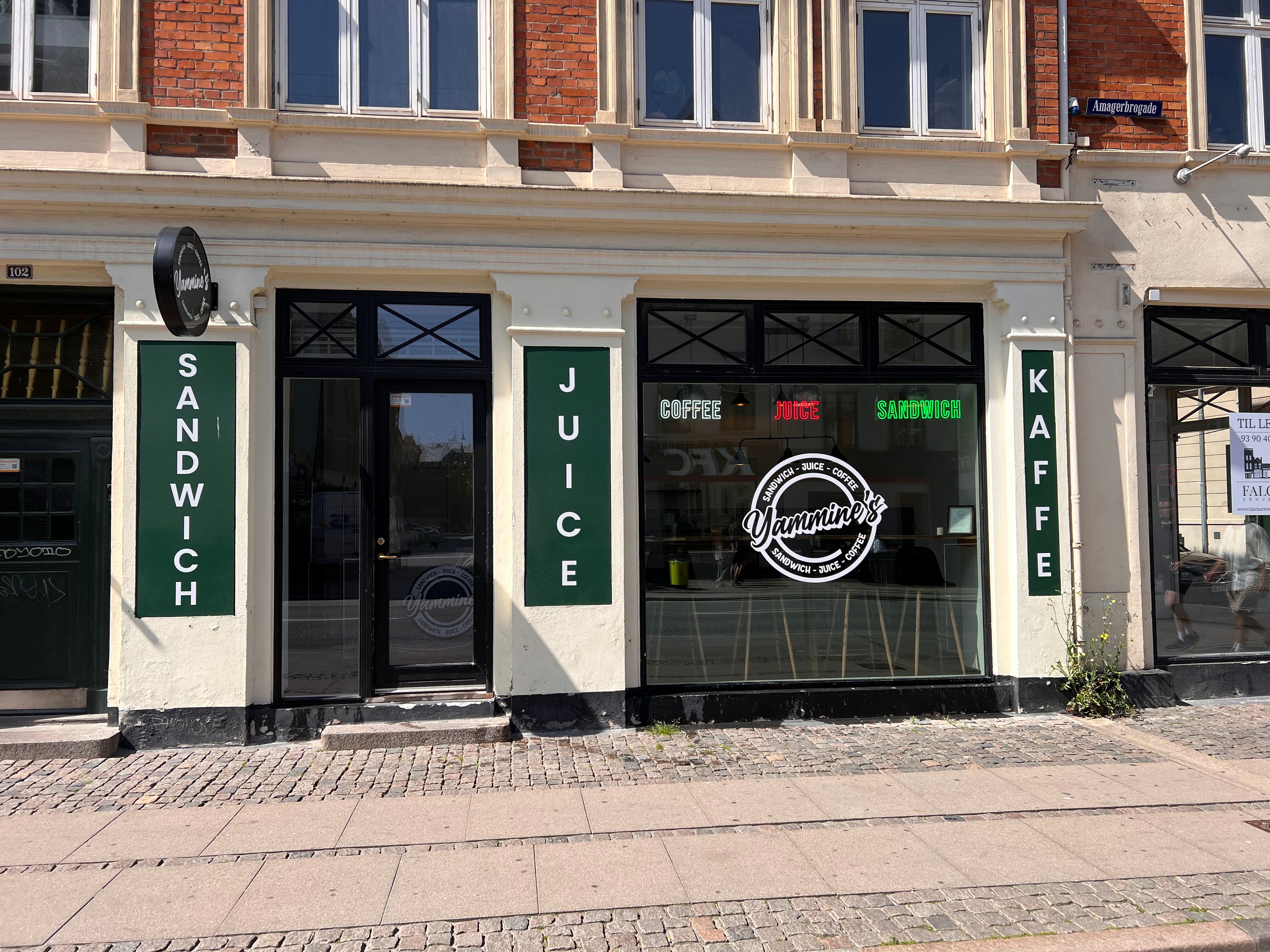Lokale med sandvich, juice og kaffe i København. Glasdøre med reklameskilte og logo.