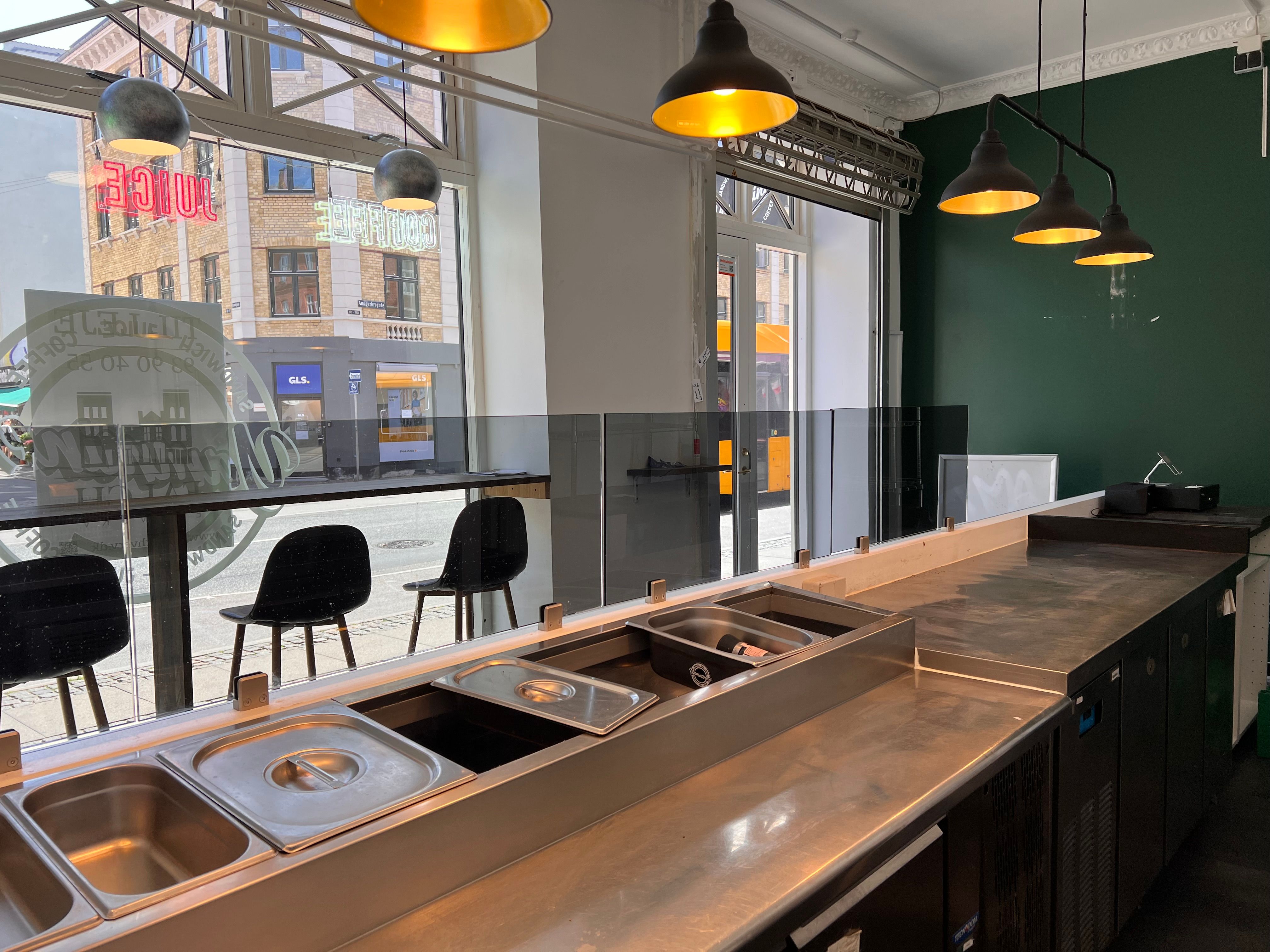 Moderne køkken med lyse blyantskuffer og glasvæg i et indbydende erhvervslokale med lyse lamper og grønne vægge