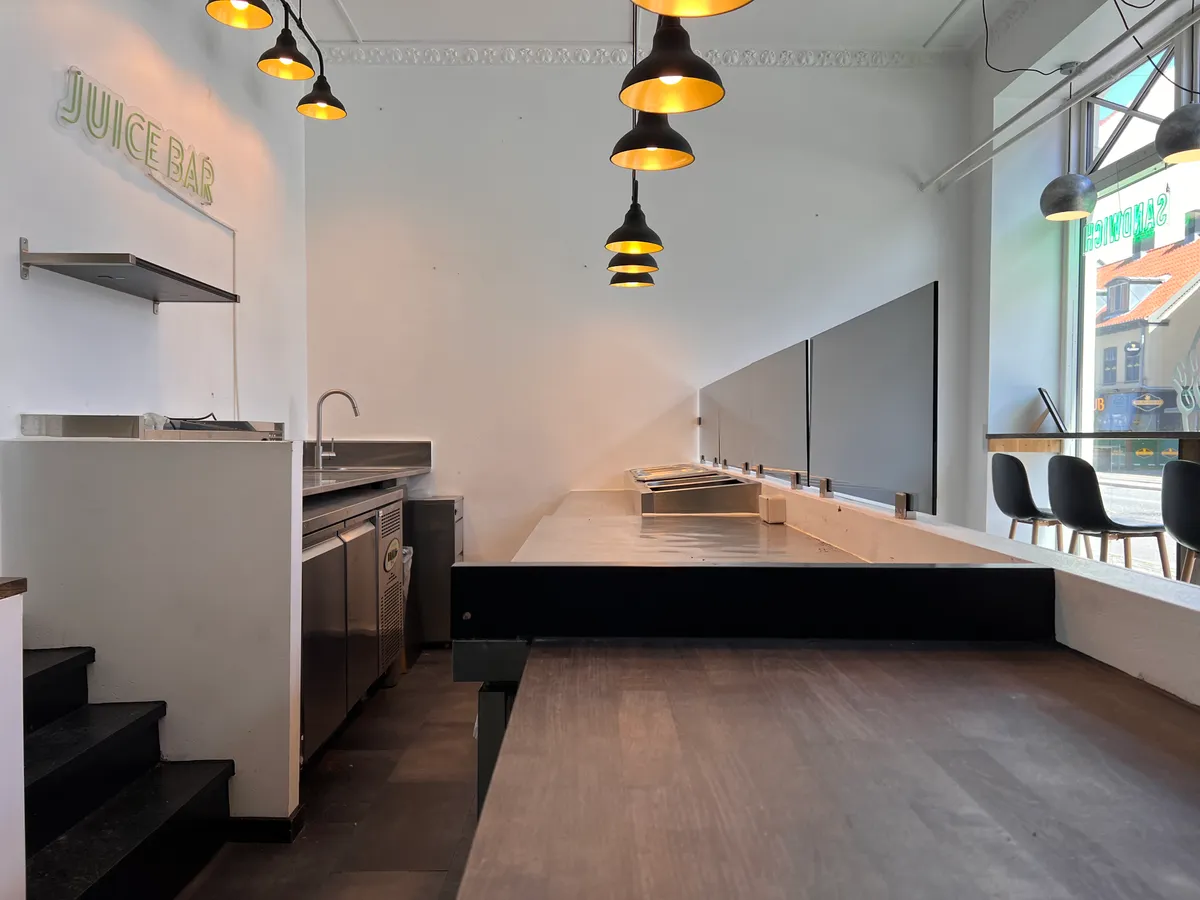 En moderne køkkenafdeling med en stor skarp skab, en høj bænk, og en lysekron med fire lyselamper hængende fra loftet