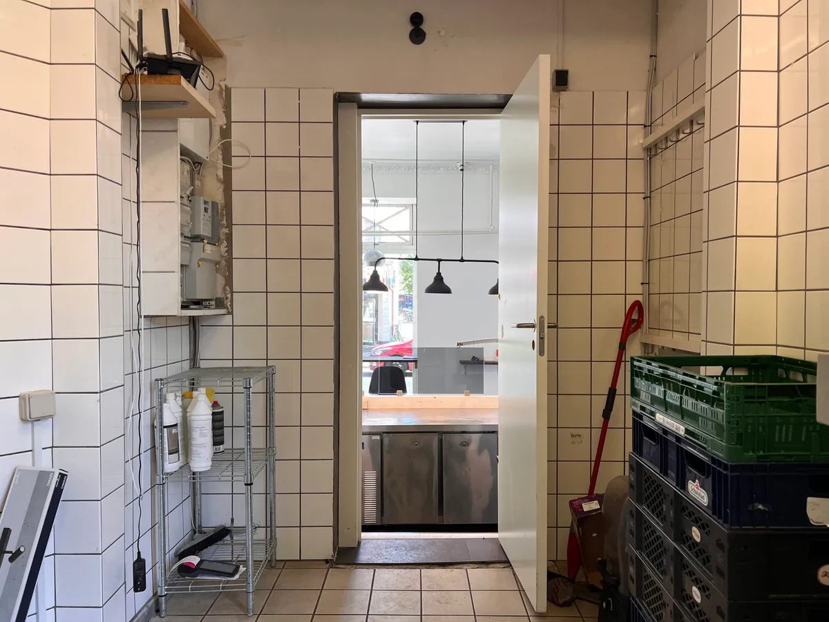En åben dør til en køkkendel med en rødt gulv og flere apparater samt flere kasser og renseriudstyr placeret på gulvet