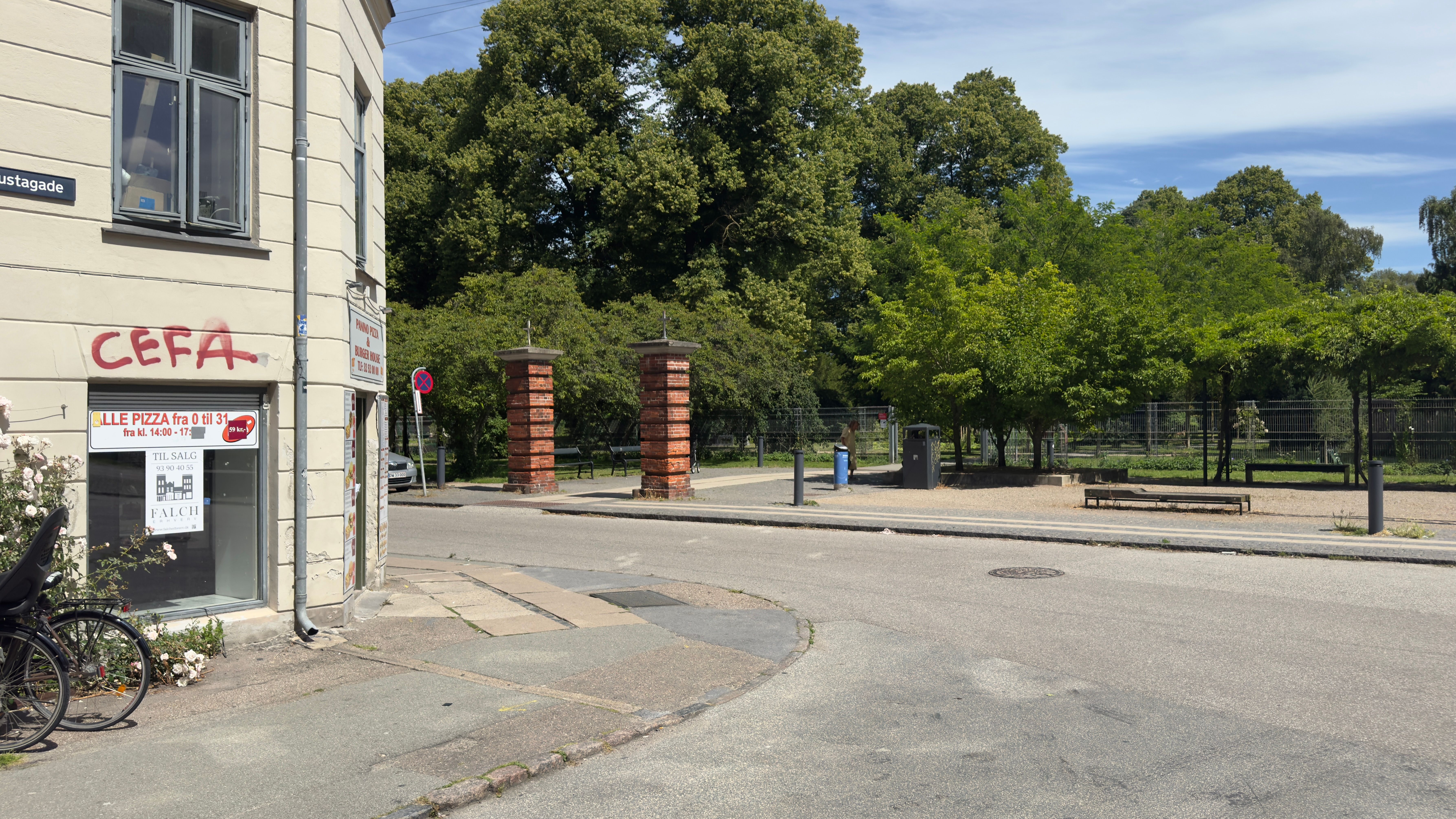 Lejlighedsvis graffiti på facaden og røde byggesten med søjler og parkbænke bagved er en pizzarestaurant med facadevinduer