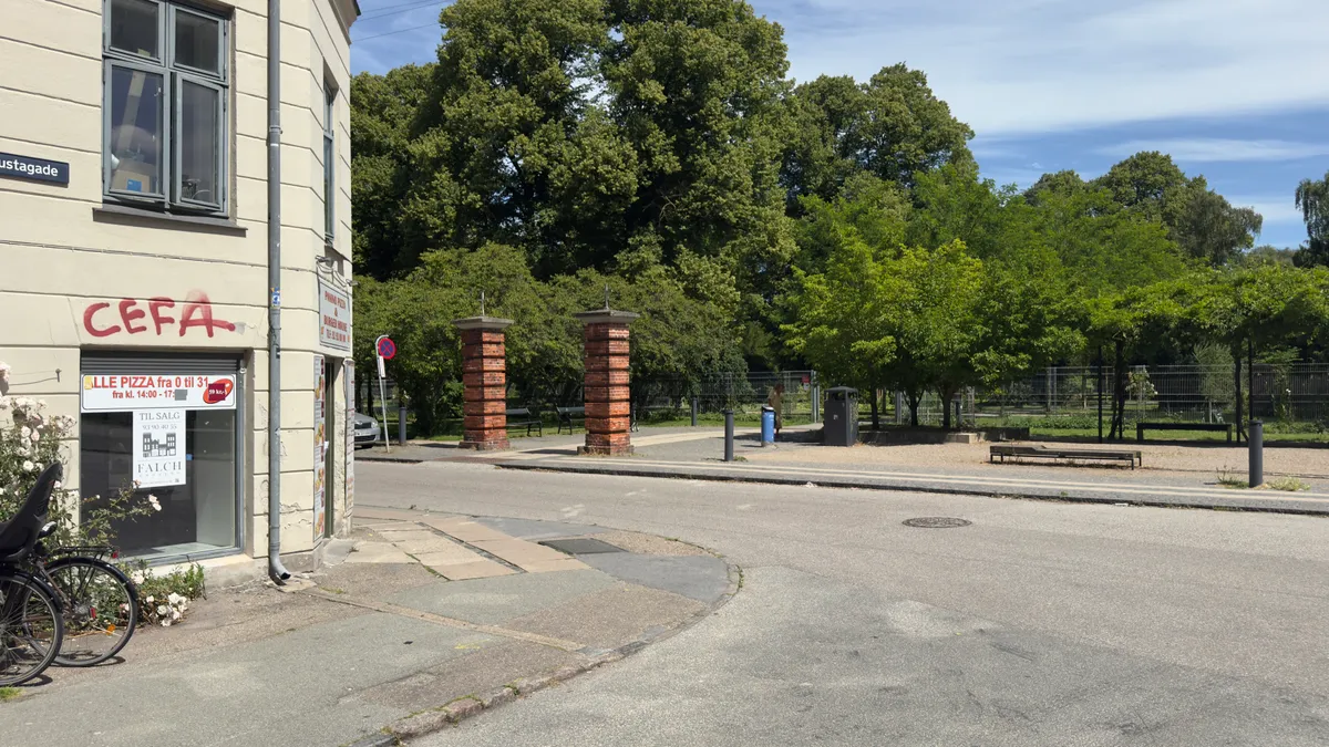 Lejlighedsvis graffiti på facaden og røde byggesten med søjler og parkbænke bagved er en pizzarestaurant med facadevinduer