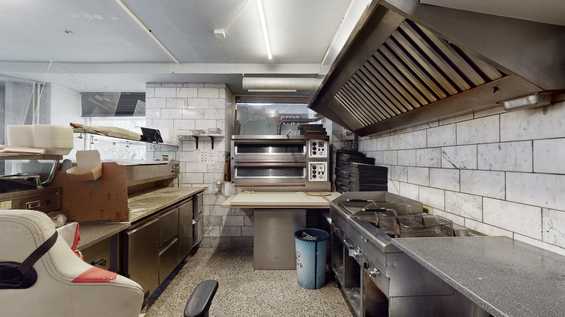 Pizzarestaurant med ovne, arbejdsborde og skraldespande i et fuldt funktionsdygtigt køkken med marmorvægge og højloft