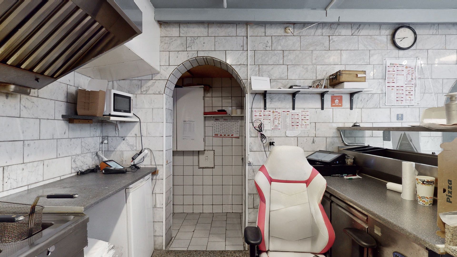 En pizzarestaurant med højt til loftet og marmorbelægning. Der er en maskine, en mikrobølgeovn og et skrivebord i nærheden.