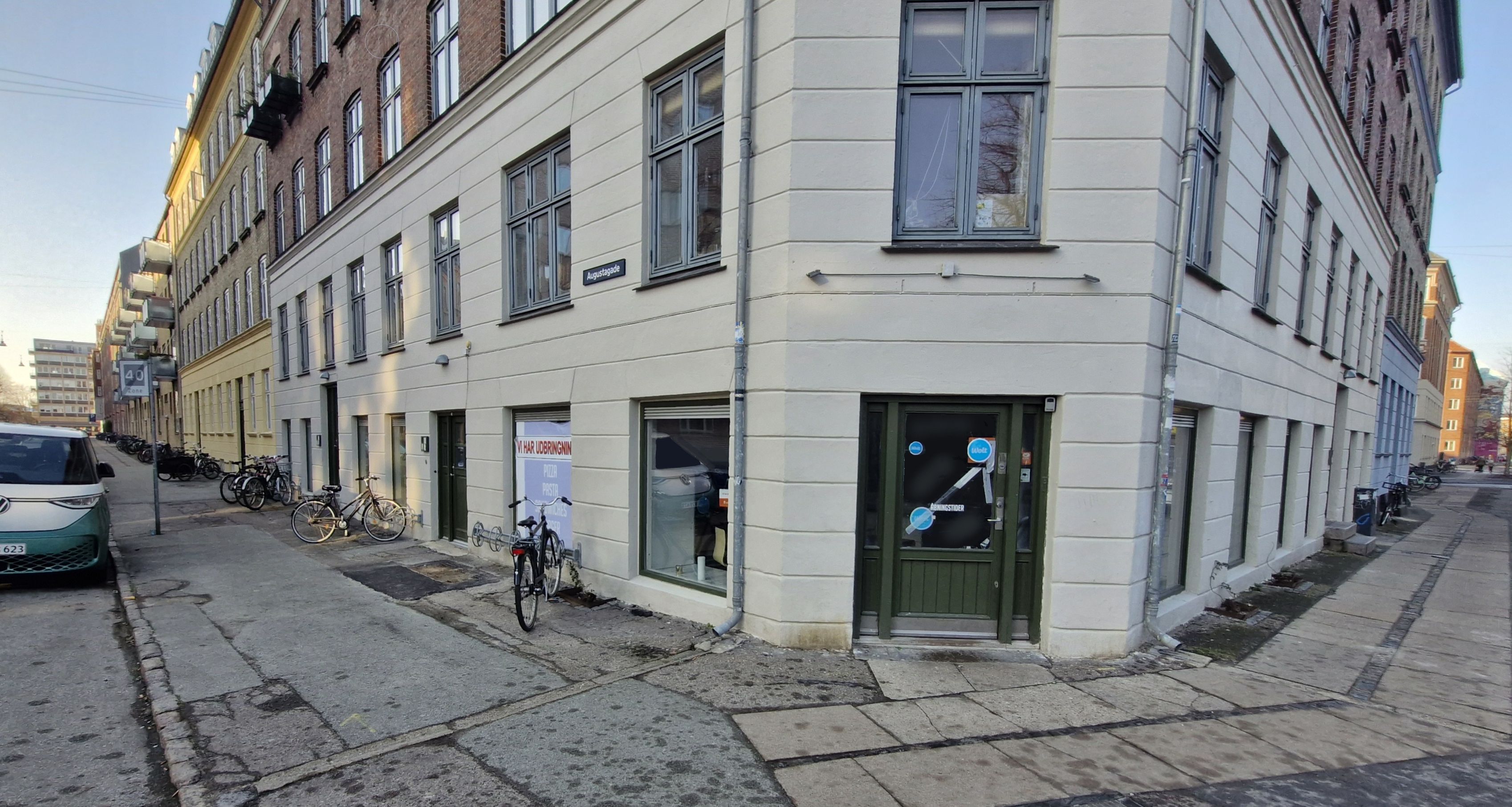 Pizzarestaurant til leje på Kirkegårdsvej 38, 2300 København S. En grøn dør med skilte og vinduer med glas og ræm. Parkerede cykler foran bygningen og en parkerede bil til venstre