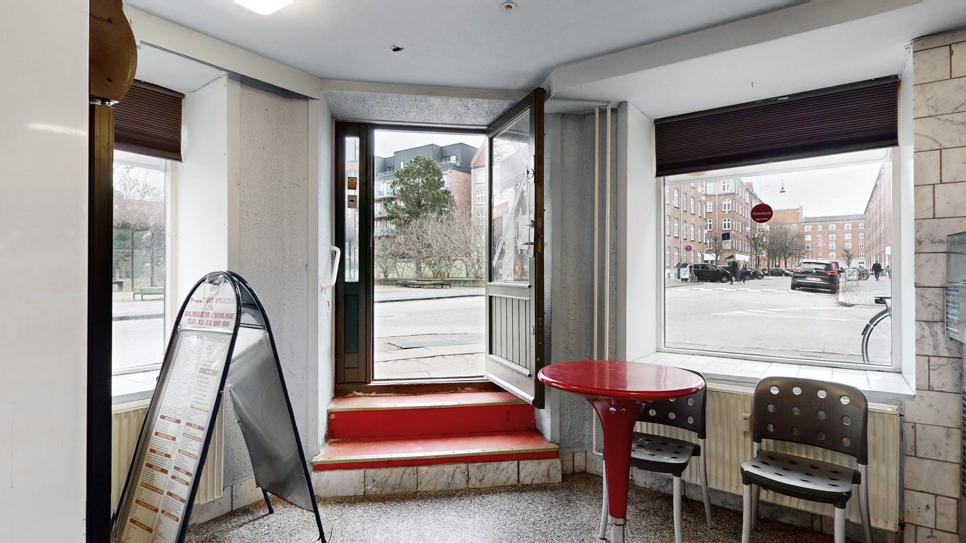 Inde i en pizzarestaurant med store vinduer og røde stolpe og bord, der vender ud mod gaden