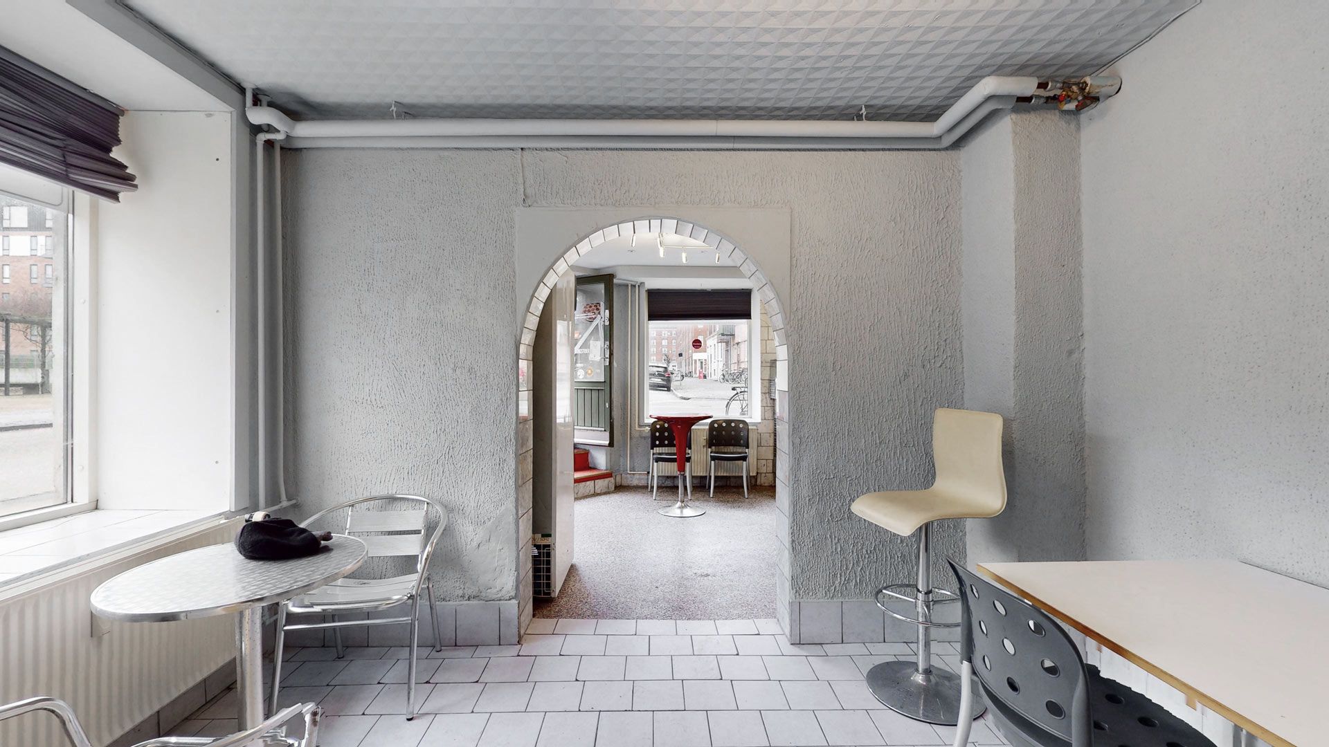 En restaurant med lyse hjørner og tydelige vinduer til gaden med en enkelt bord med en høj stol og et kaffebord med en stol